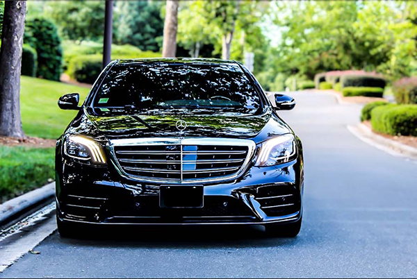 shiny black mercedes driving on quiet street with mature trees