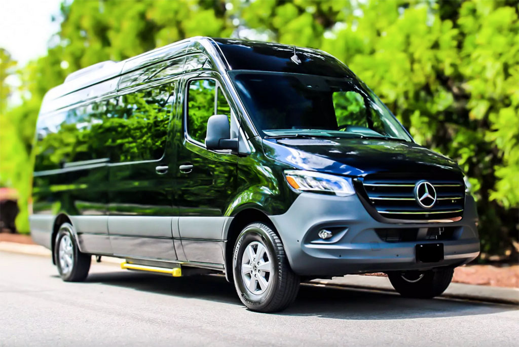 shiny black mercedes sprinter driving on quiet street with green trees in the background